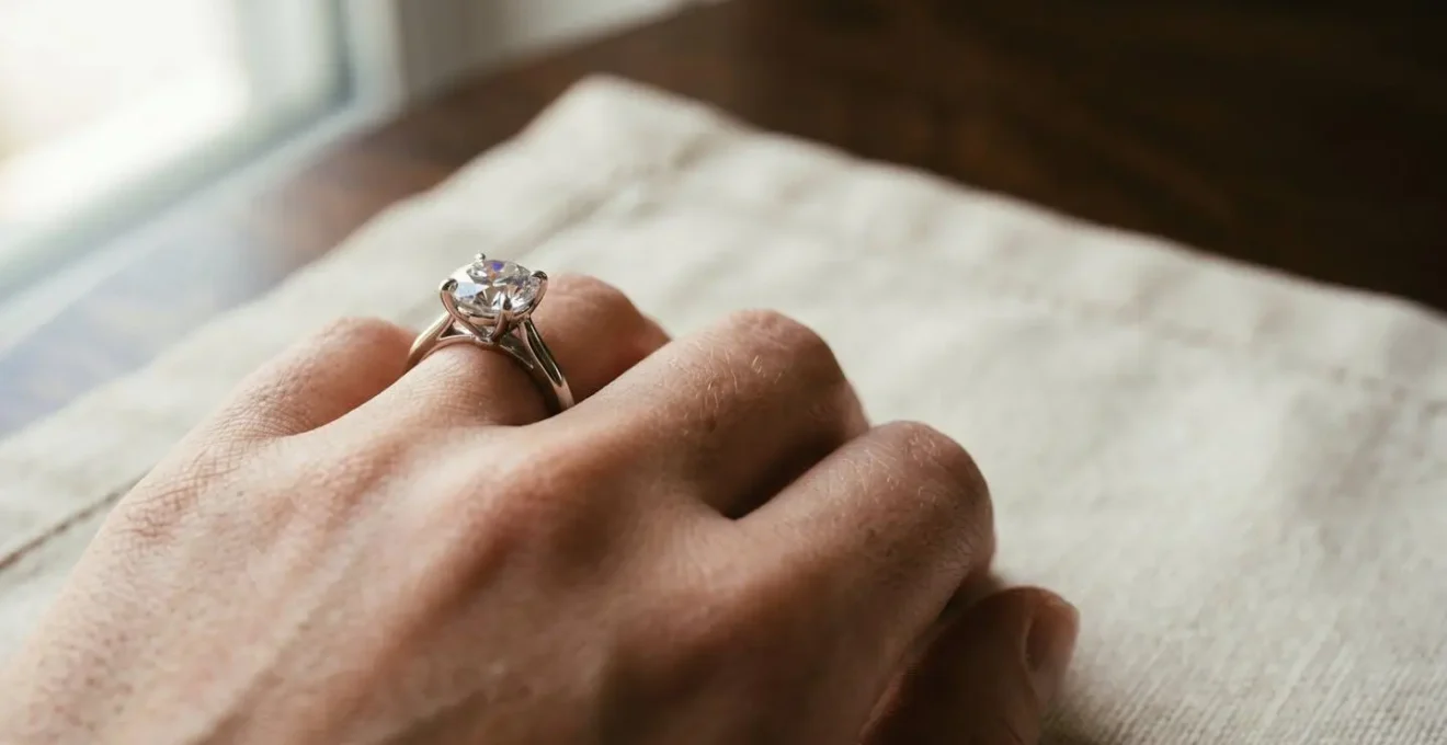 Gros plan sur une main portant une bague solitaire diamant, éclairage naturel mettant en valeur les reflets de la pierre et les détails de la monture