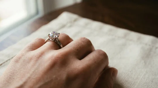 Gros plan sur une main portant une bague solitaire diamant, éclairage naturel mettant en valeur les reflets de la pierre et les détails de la monture