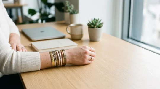 Composition élégante de plusieurs bracelets joncs métalliques empilés sur un poignet au bureau, jeu de textures lisses et martelées, lumière naturelle douce